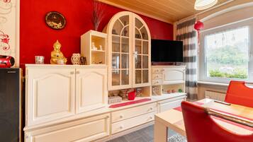 Ein Zimmer mit einer roten Wand, einem weißen Schrank mit Glastüren, einem Fernseher und einem roten Sessel.