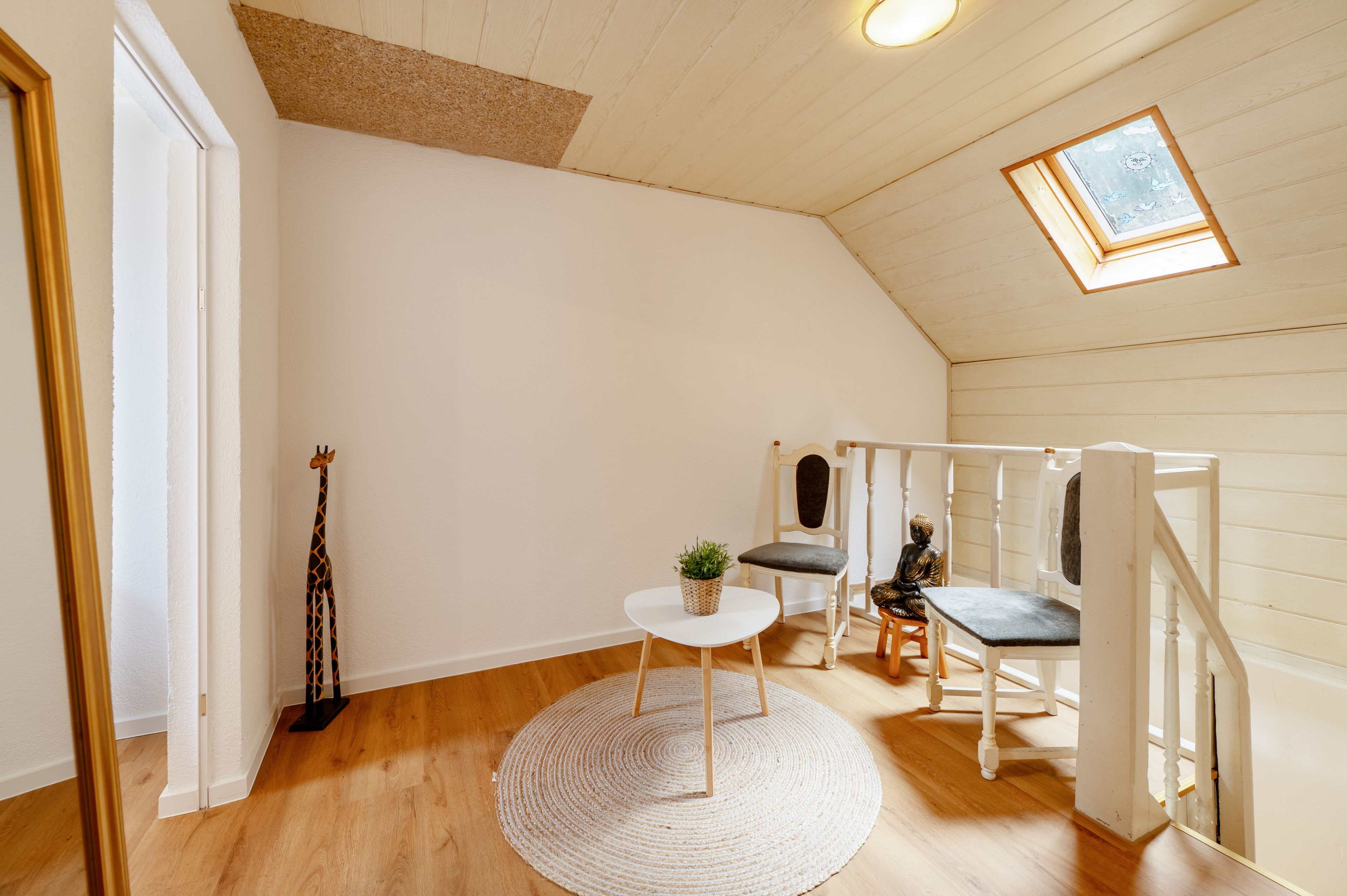 A room with a sloped ceiling, a small table with a plant, a chair, and a statue.