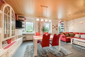 A cozy living room with a red sofa, a dining table with chairs, a TV, and a bookshelf.