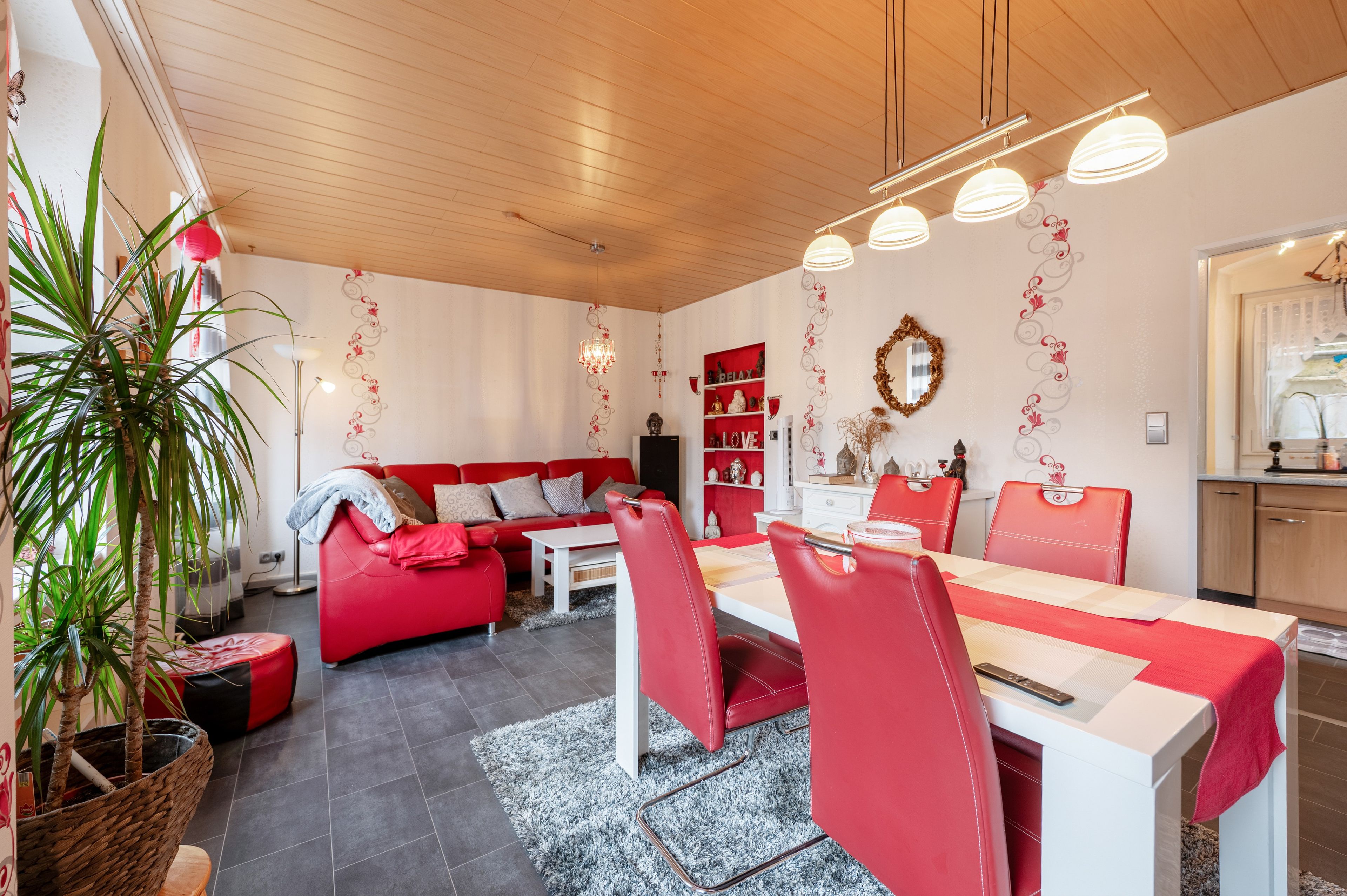 Un soggiorno moderno con un divano rosso, un tavolino da caffè bianco e poltrone rosse abbinate. Si nota un lampadario, una libreria rossa e uno specchio decorativo a parete.