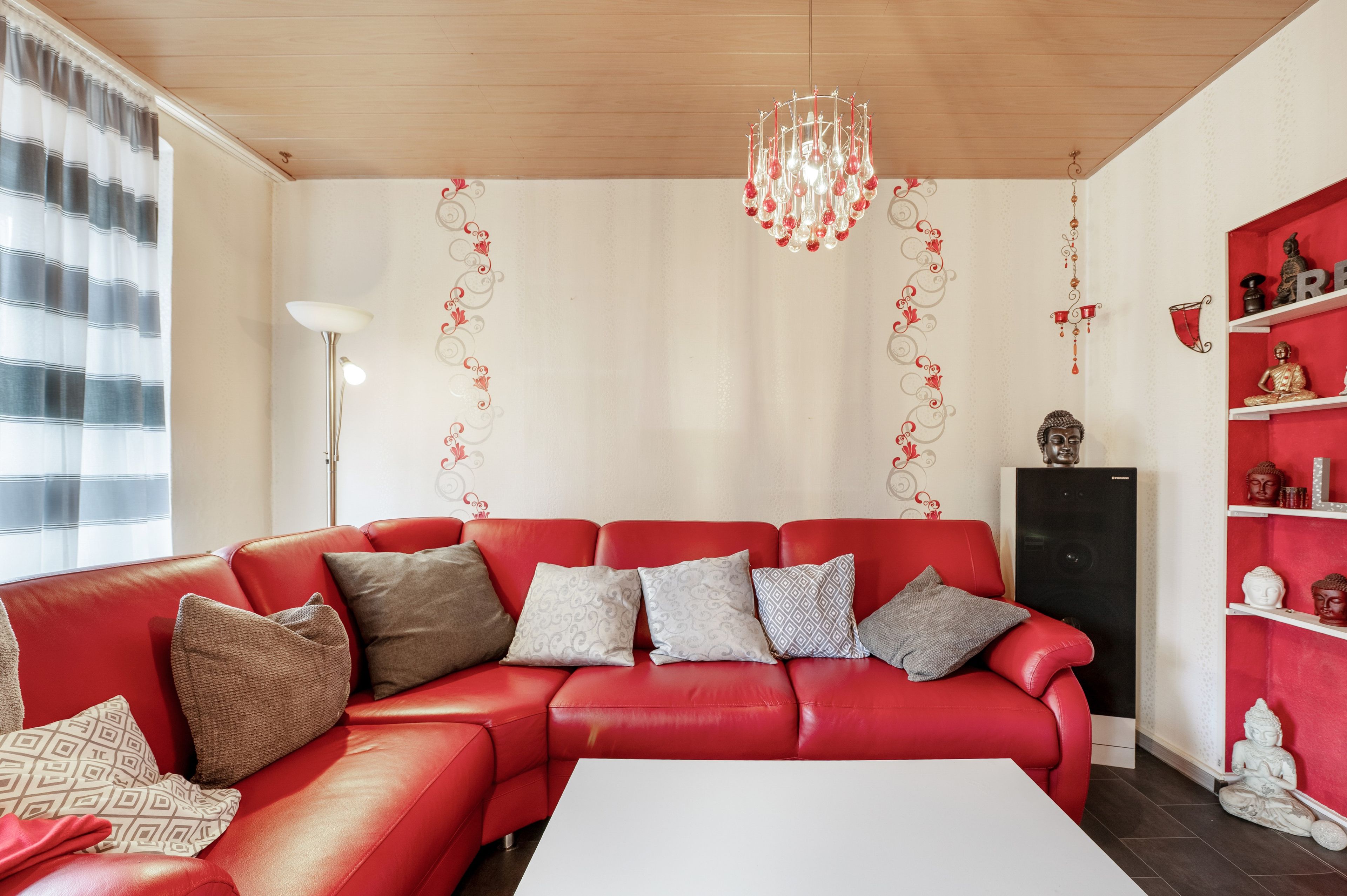 A red leather sofa with patterned cushions, a white coffee table, and a decorative chandelier.