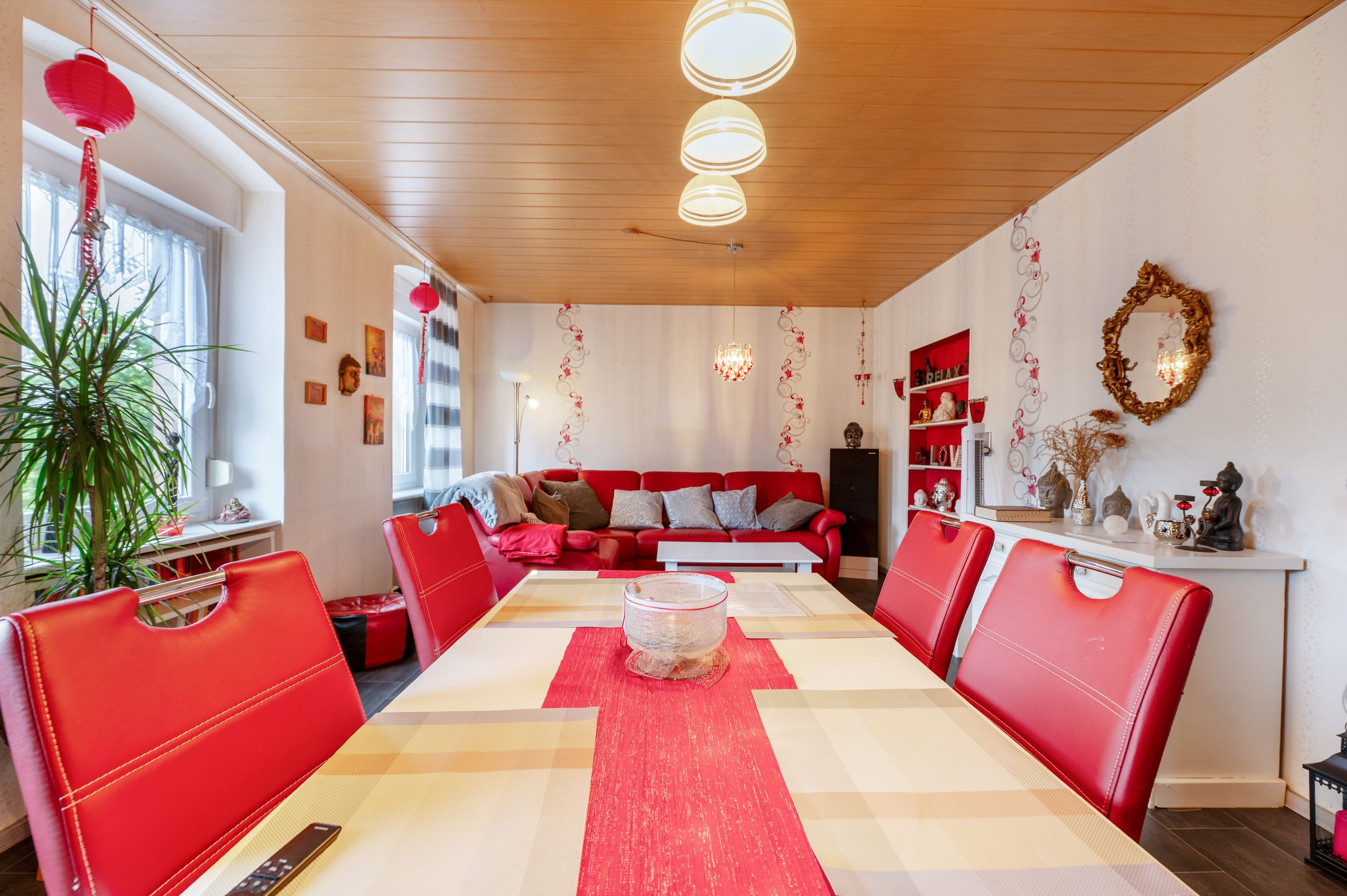 Ein Essbereich mit einem roten und beigen Tisch, roten Stühlen, einer Chandelier und einem roten Laterne.