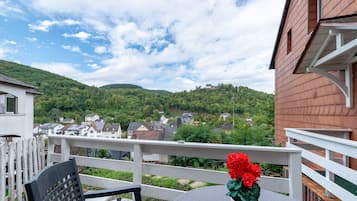 A balcony with a view of a hillside village, a white railing, and a table with a chair.