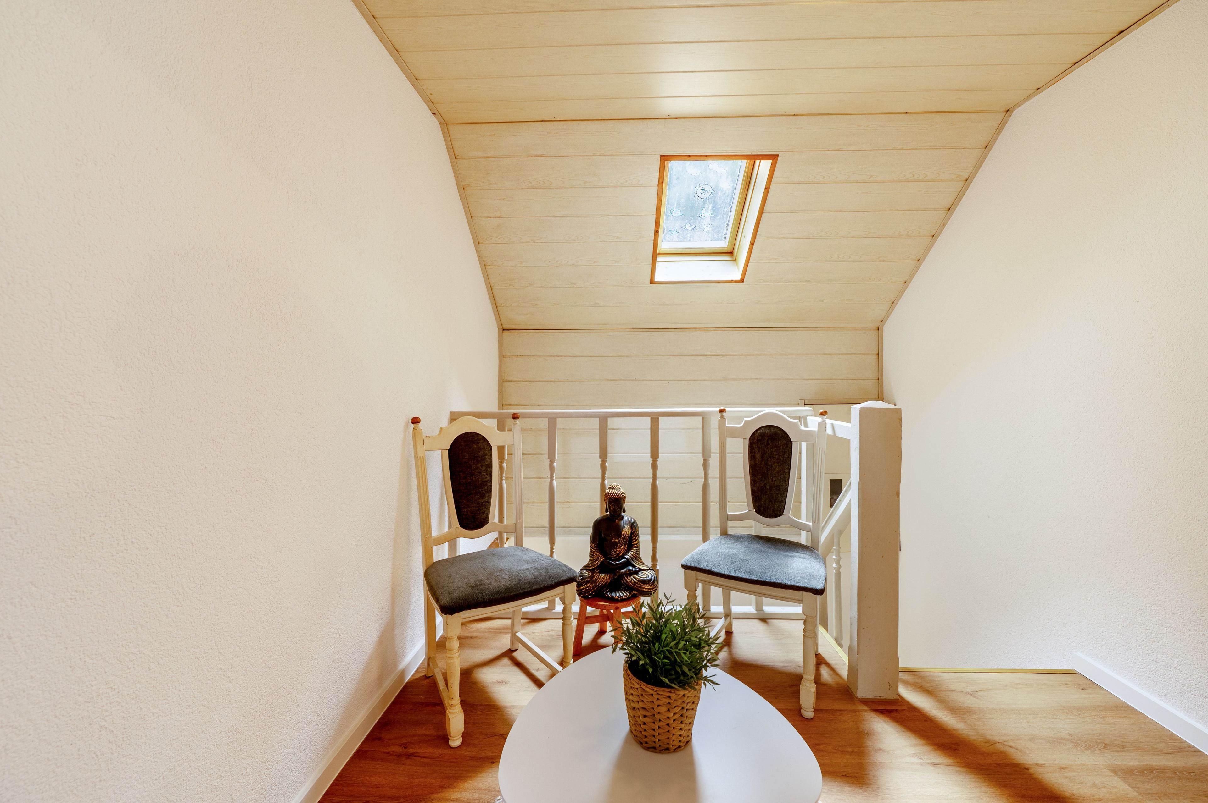Une petite pièce agréable, avec un plafond en pente, deux chaises, une table et une plante en pot.
