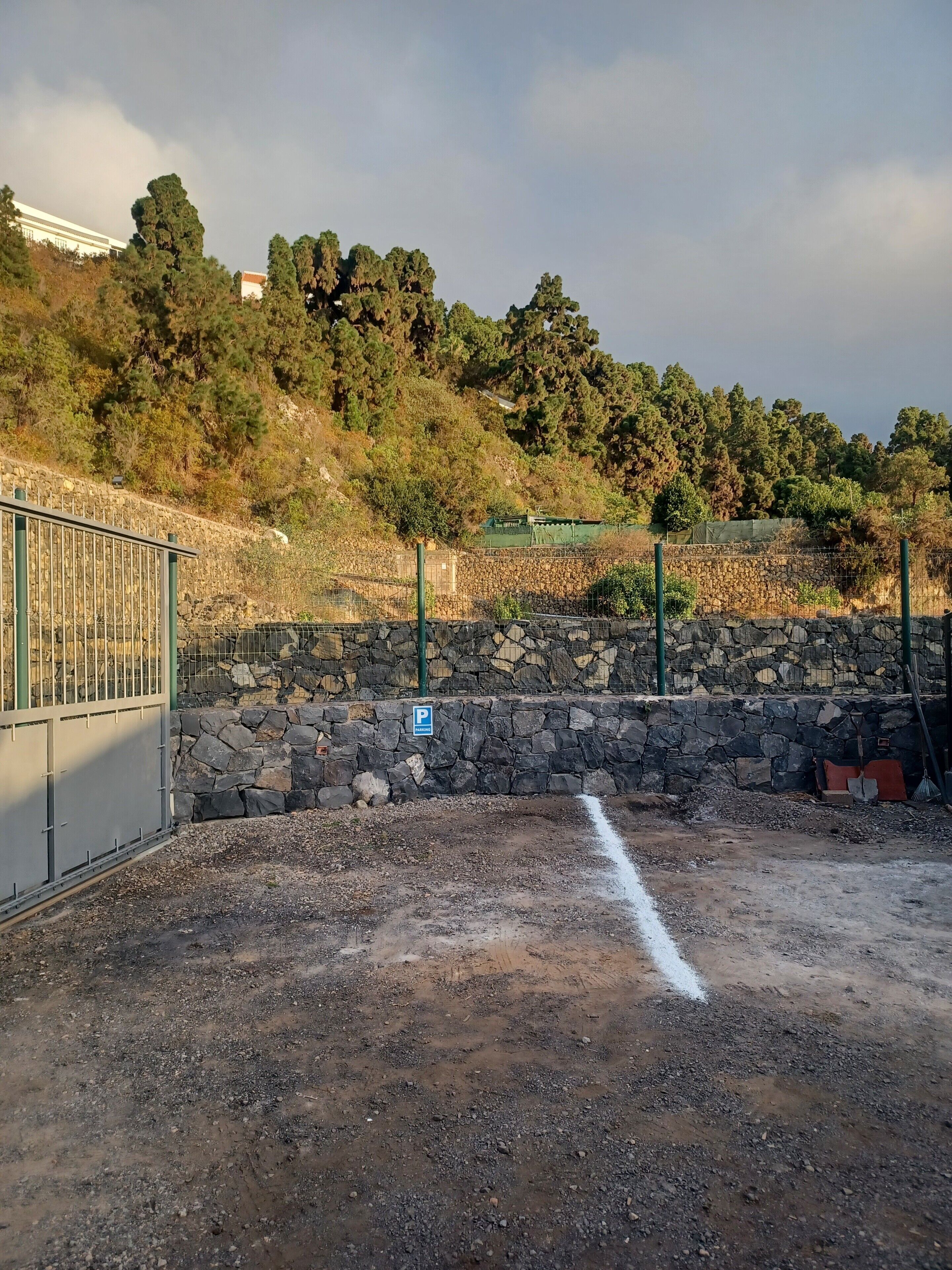 A gravel parking area with a stone wall and a metal fence.
