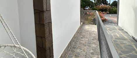 A stone-tiled balcony with a white chair and a metal railing.