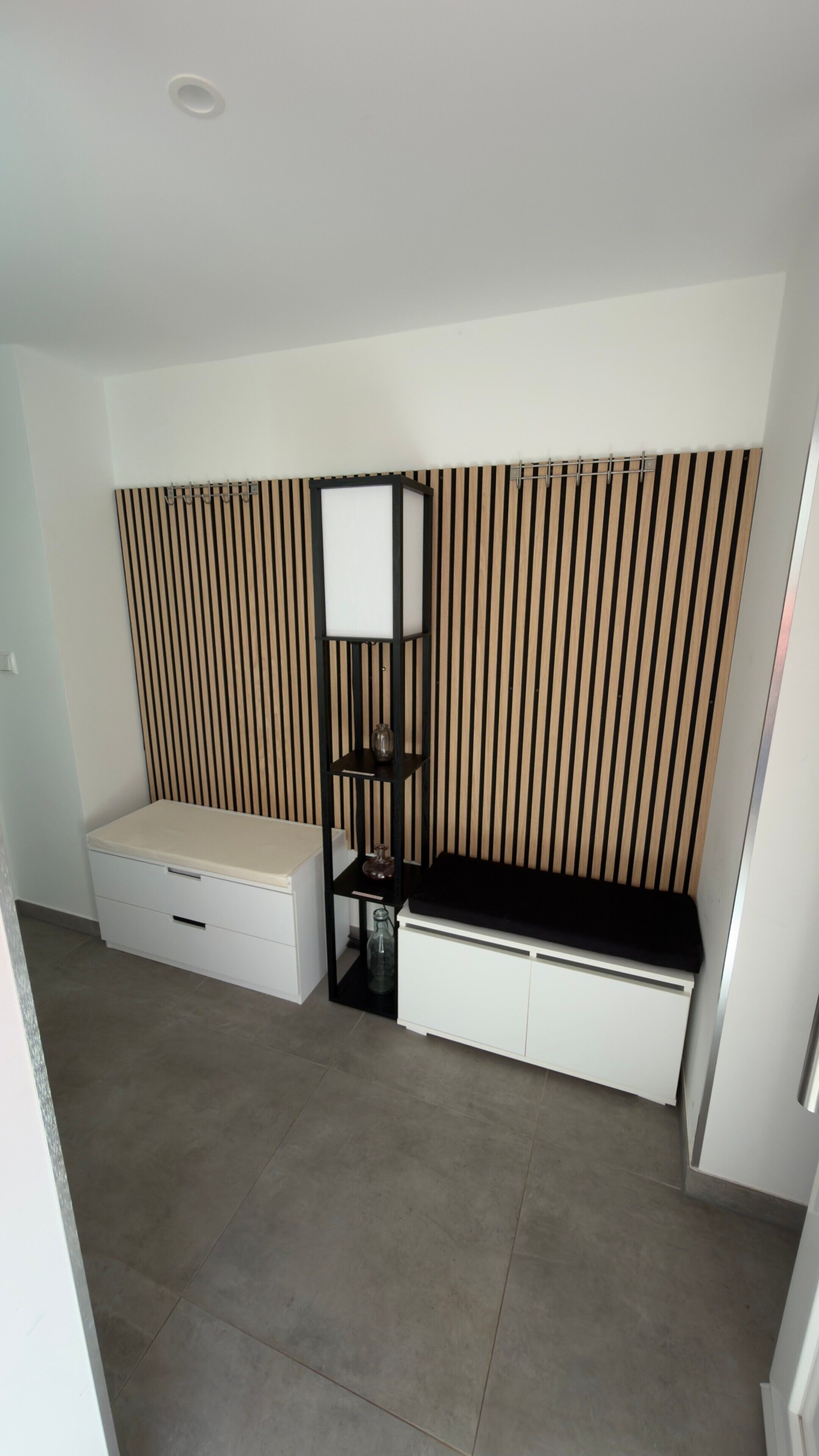 Een kamer met een bed, een klein wit kastje en een wandplank tegen een gestreepte muur.
