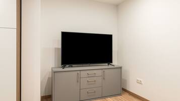 Une pièce moderne et minimaliste, dotée d’un téléviseur à écran plat fixé sur un meuble gris, d’un plancher en bois et de murs blancs.