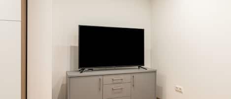 Une pièce moderne et minimaliste, dotée d’un téléviseur à écran plat fixé sur un meuble gris, d’un plancher en bois et de murs blancs.