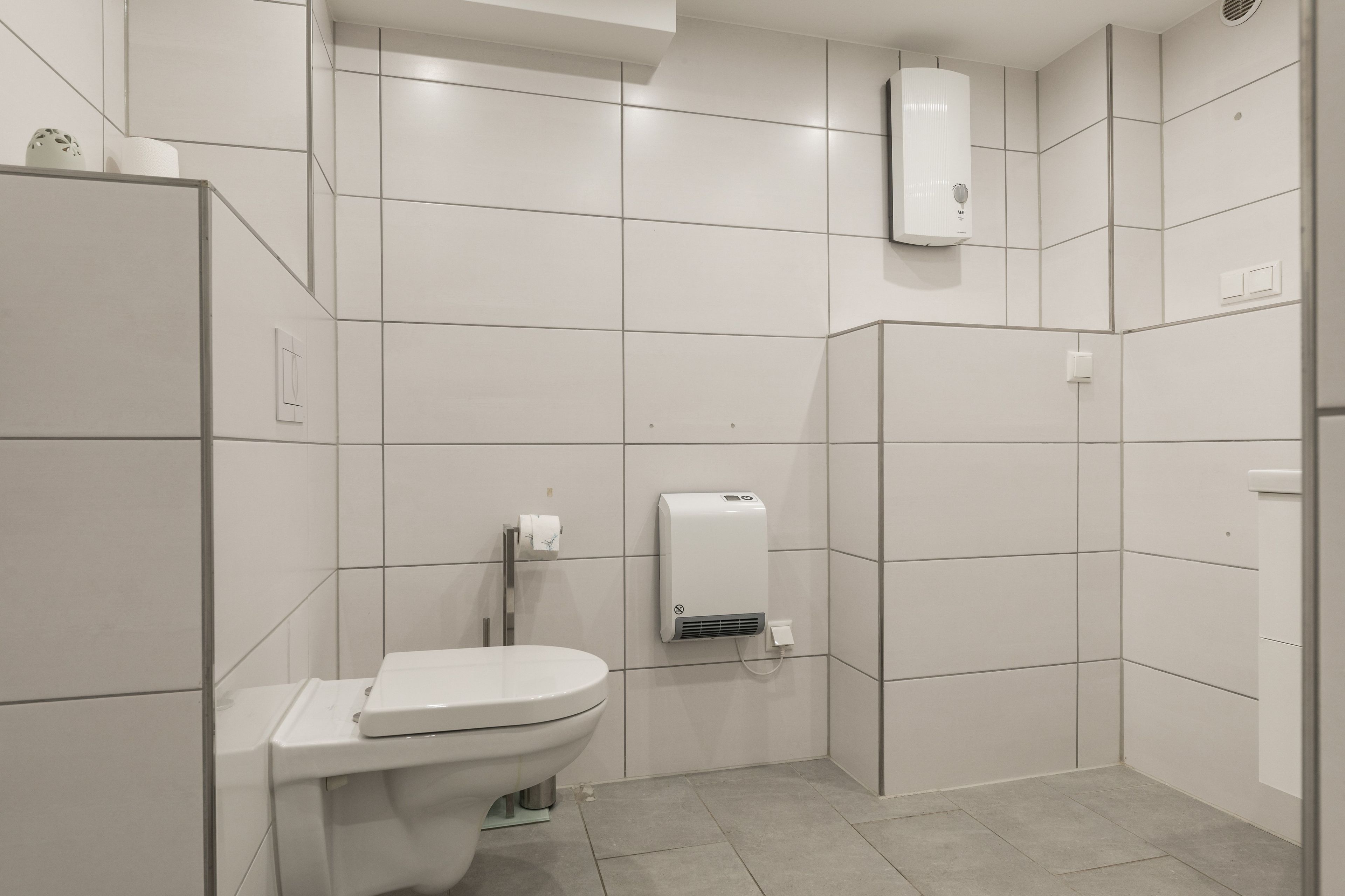 A modern bathroom with a toilet, a hand dryer, and a wall-mounted air conditioning unit.