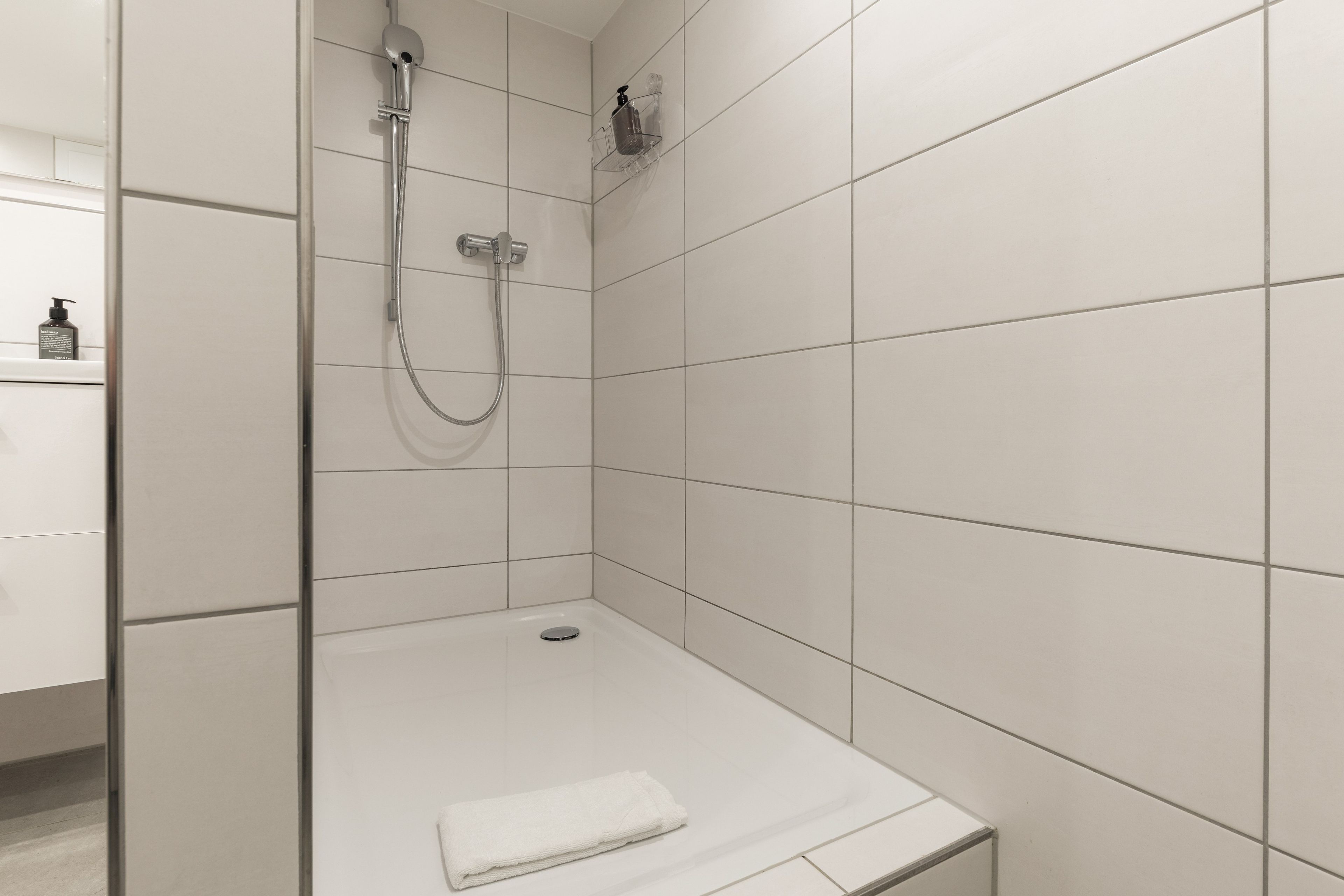 A modern bathroom with a glass shower enclosure, a white sink, and a towel on the floor.