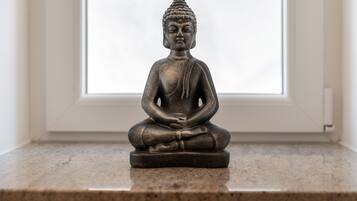 A statue of a seated figure on a pedestal in a room with a window.