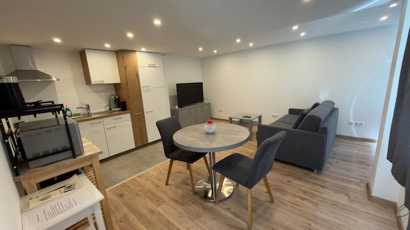 Un espacio habitable compacto con kitchenette, comedor y zona de estar.