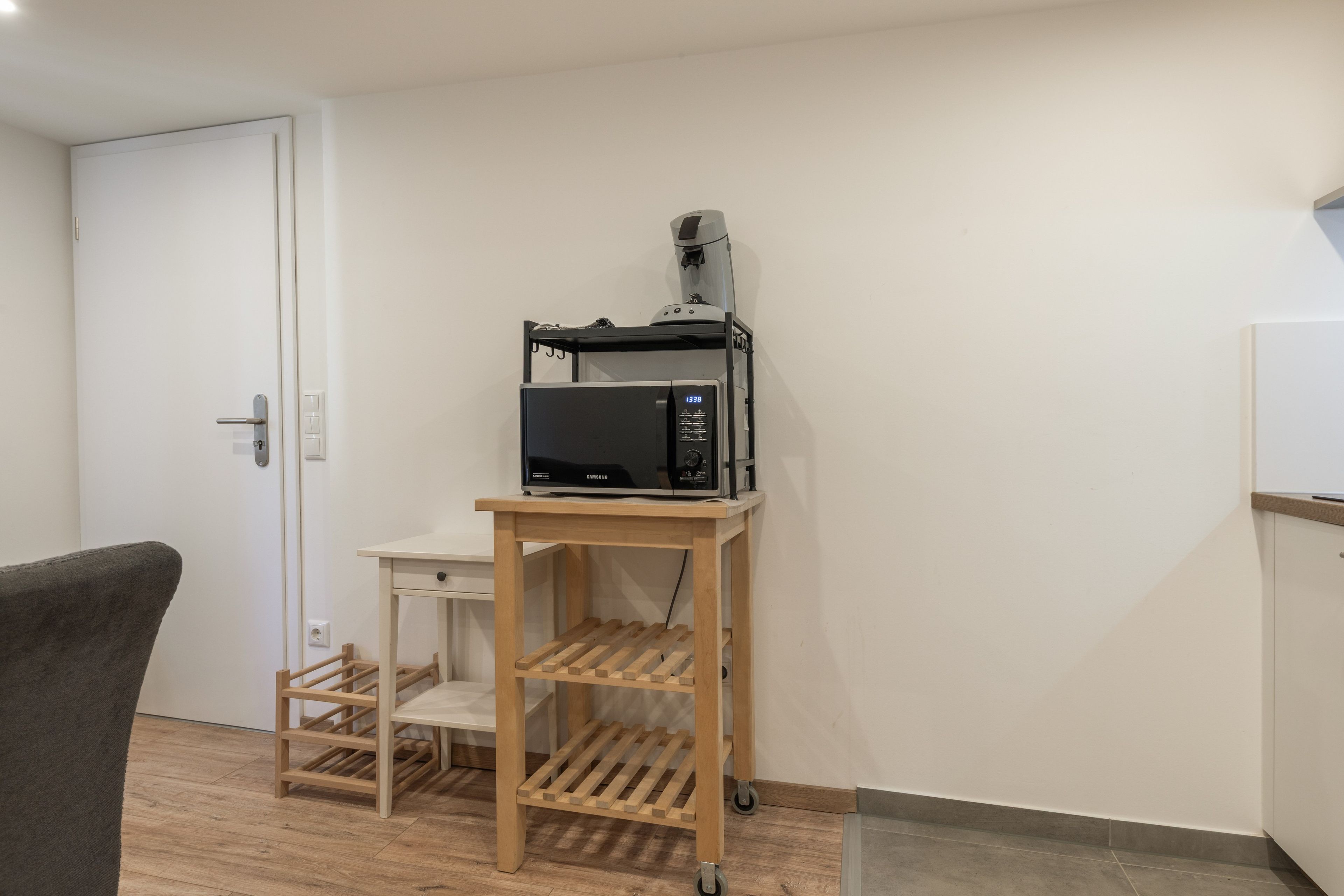 A room with a microwave on a wooden cart, a door, and a chair.