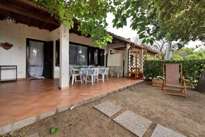 A covered patio area with a table and chairs, a bench, and a small garden. - Casa Lalla - Costa Rei: Holiday Home Near the Beach with Garden and Sea View (Costa Rei)