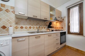 A kitchen with a sink, stove, and oven. There are cabinets and a window with curtains. - Casa Lalla - Costa Rei: Holiday Home Near the Beach with Garden and Sea View (Costa Rei)