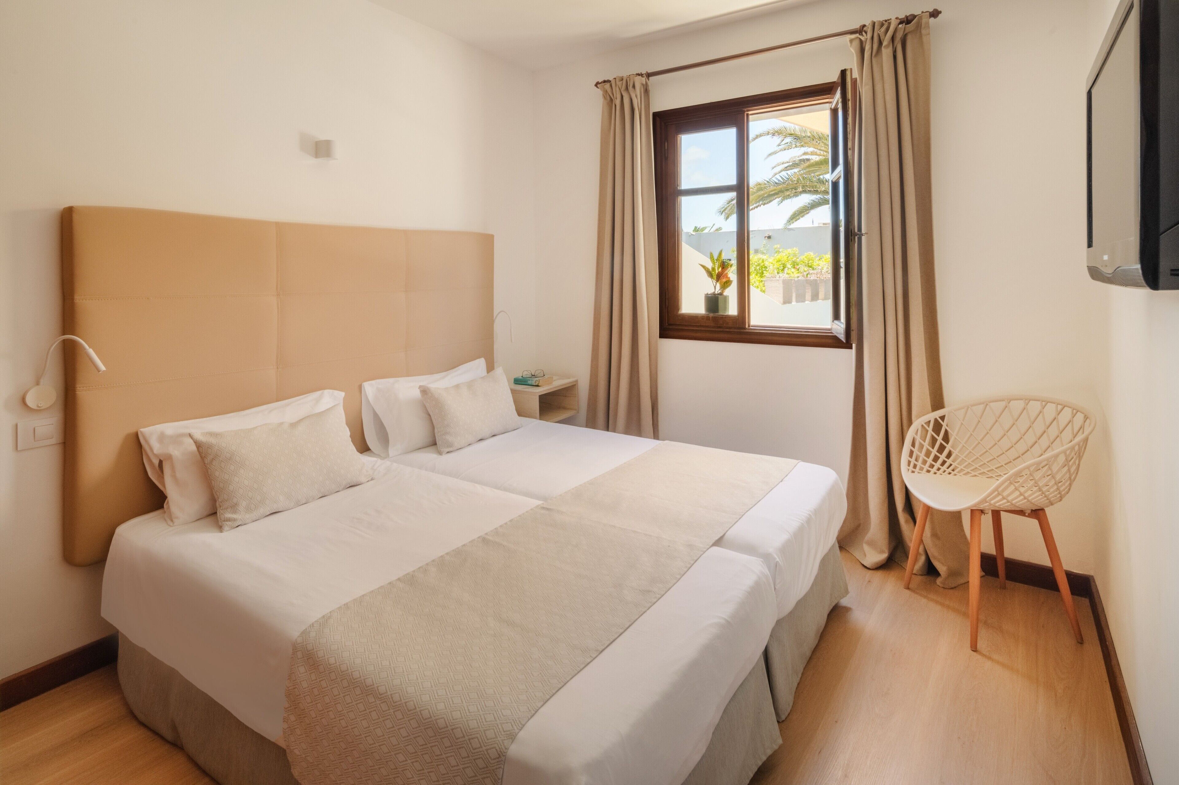A hotel room with a large bed, a bedside table, a chair, and a window with curtains.