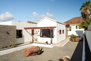 Ein modernes Haus mit weißer Fassade, einer Steinsäule links und einem großen Felsen im Vordergrund.