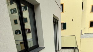 En smal udendørs gang med flisegulv, et vindue med sort ramme og en dør med grøn lukke