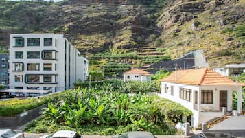 Un bâtiment moderne à la façade blanche et aux grandes fenêtres, entouré d’une végétation luxuriante et d’un paysage vallonné.