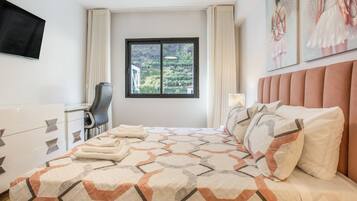 A hotel room with a bed, a desk, a chair, and a window with a view of greenery.