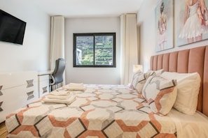 Een hotelkamer met een bed, een bureau, een stoel en een raam met uitzicht op groen.