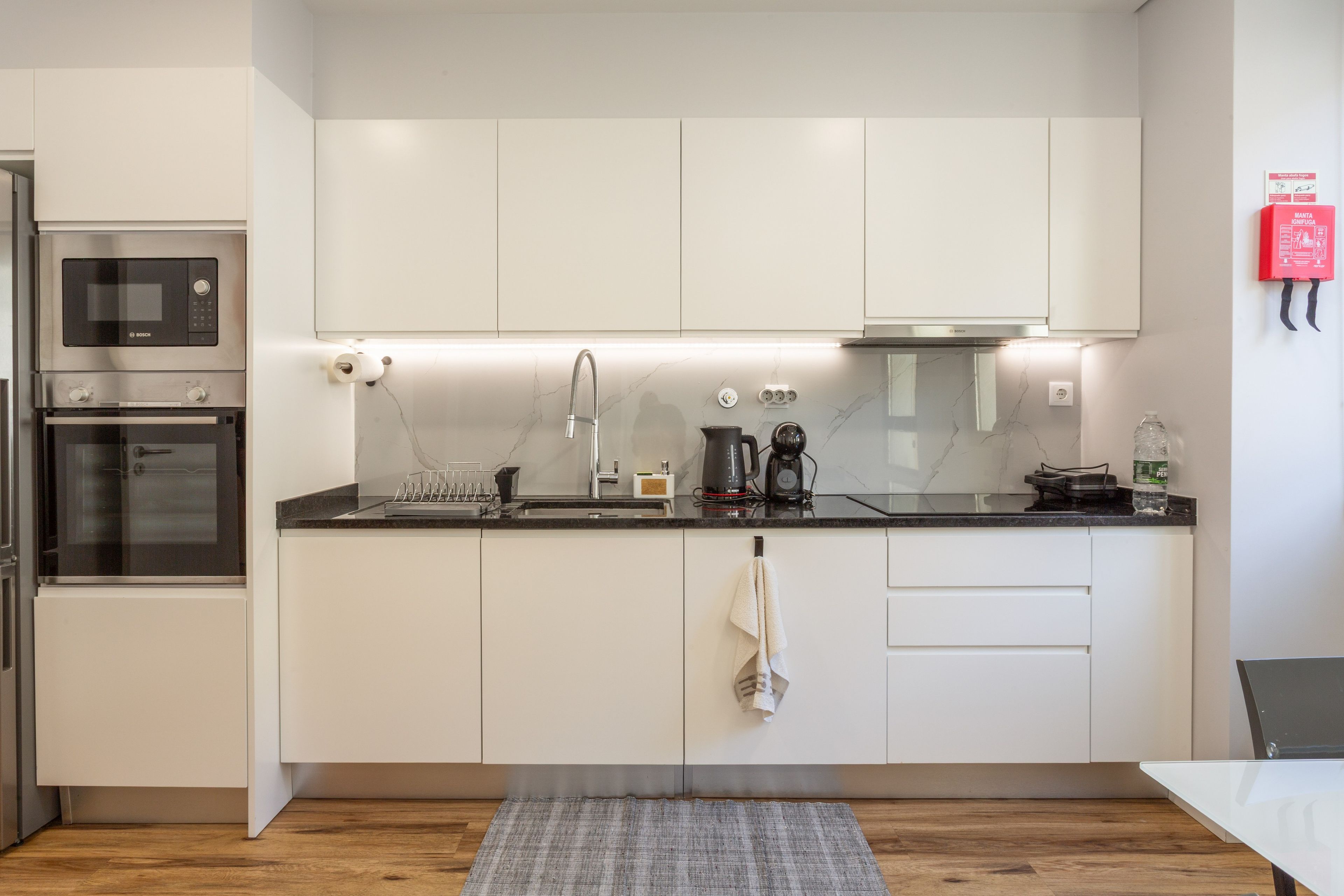Een moderne keuken met witte kasten, een Bosch magnetron, een waterkoker en een waterdispenser.