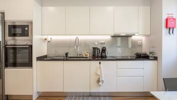 Een moderne keuken met witte kasten, een Bosch magnetron, een waterkoker en een waterdispenser.