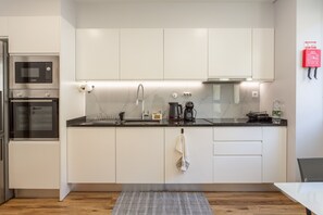 A modern kitchen with white cabinetry, a Bosch microwave, a kettle, and a water dispenser. - Visconde II F Apartment - Ribeira Brava (Ribeira Brava)