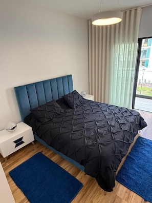 Ein modernes Schlafzimmer mit einem großen Bett, einem Nachttisch und einem Fenster mit Vorhängen.