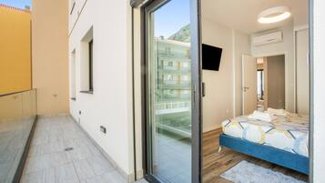 Un dormitorio moderno con un vidrio que da a un balcón, una cama con cubrecama estampado y un televisor montado en la pared.