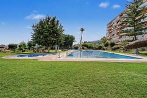 A swimming pool surrounded by grass, trees, and a building with balconies.