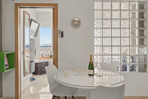 A room with a round glass table, two chairs, a bottle of champagne, and a view through a window with a decorative grille.