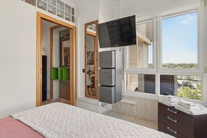 A bedroom with a bed, a TV, a window with a view, and a door leading to a bathroom.