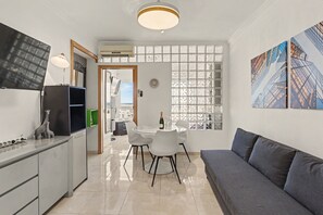 Een moderne keuken met een eethoek, een bank en uitzicht op gebouwen door een raam.
