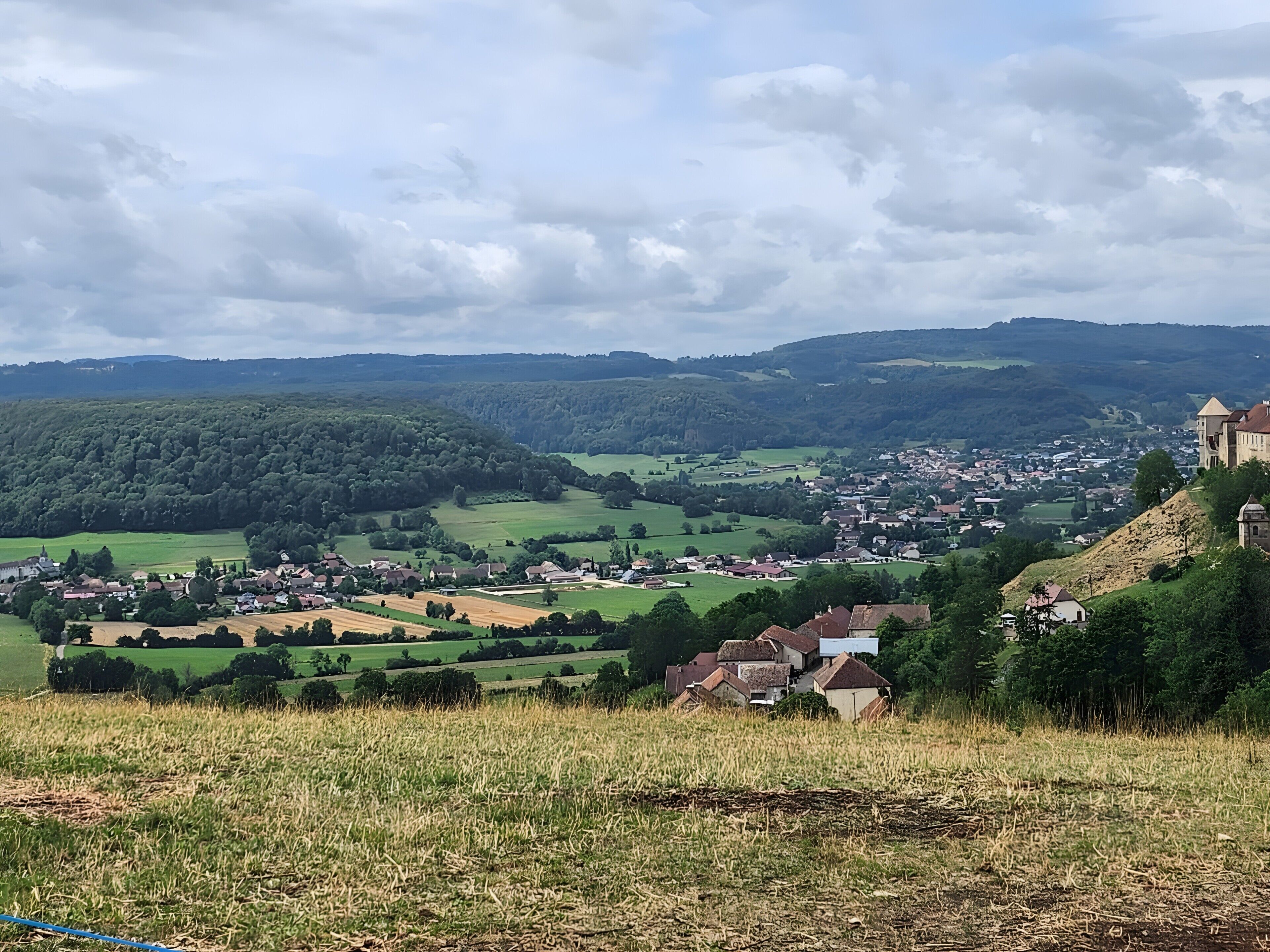 Een landelijk landschap met een dorp, velden en een heuvel met een gebouw.