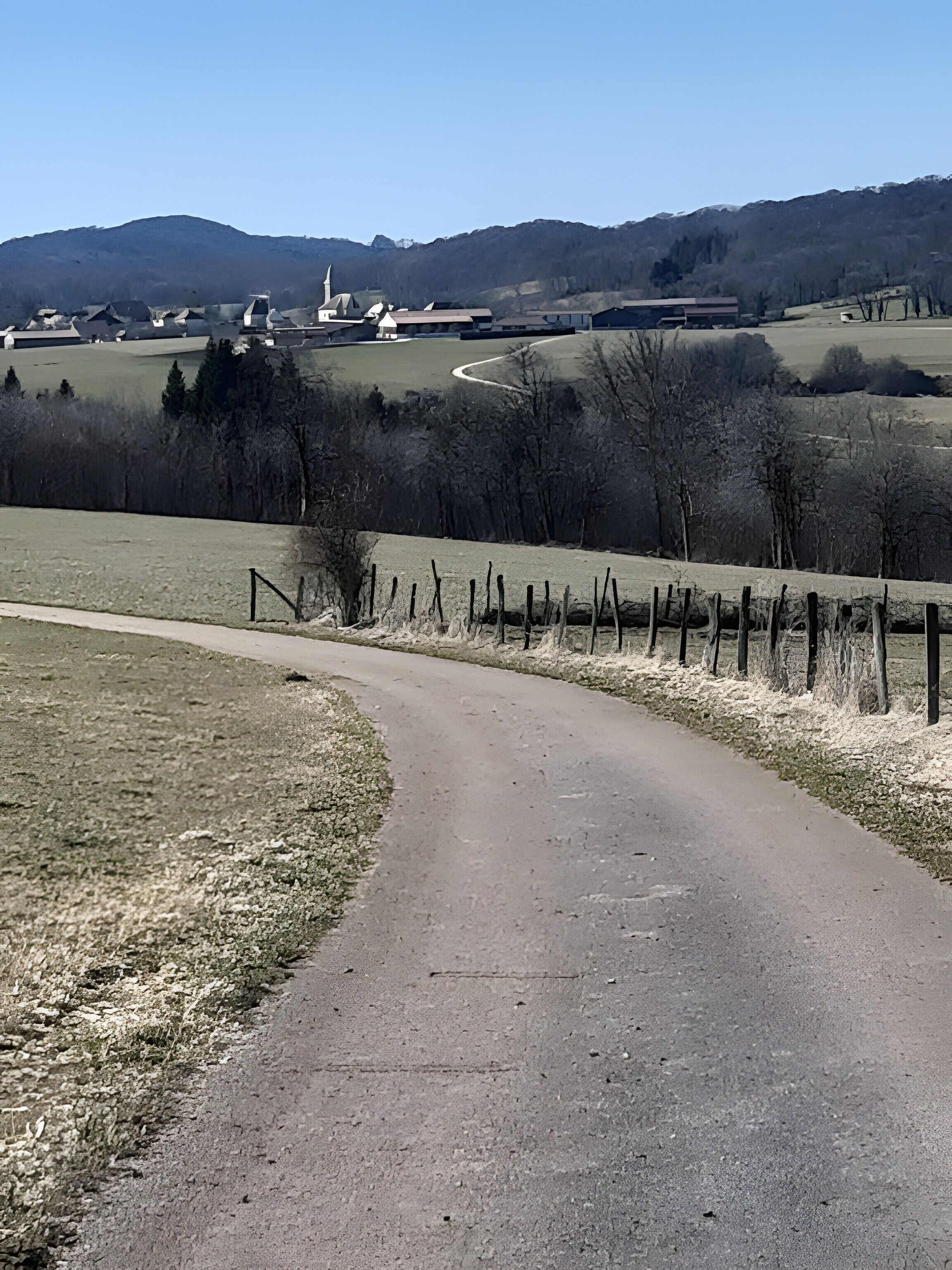 A rural road curving through a landscape with a church and open fields in the distance.