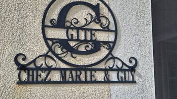 Een metalen bord met de tekst 'CHEZ MARIE & GUN' op een structuurrijke muur.