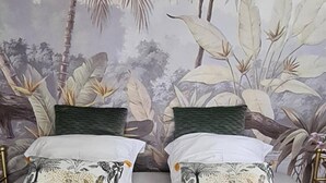 Une chambre avec un lit adossé à un mur orné d’une fresque aux motifs tropicaux.