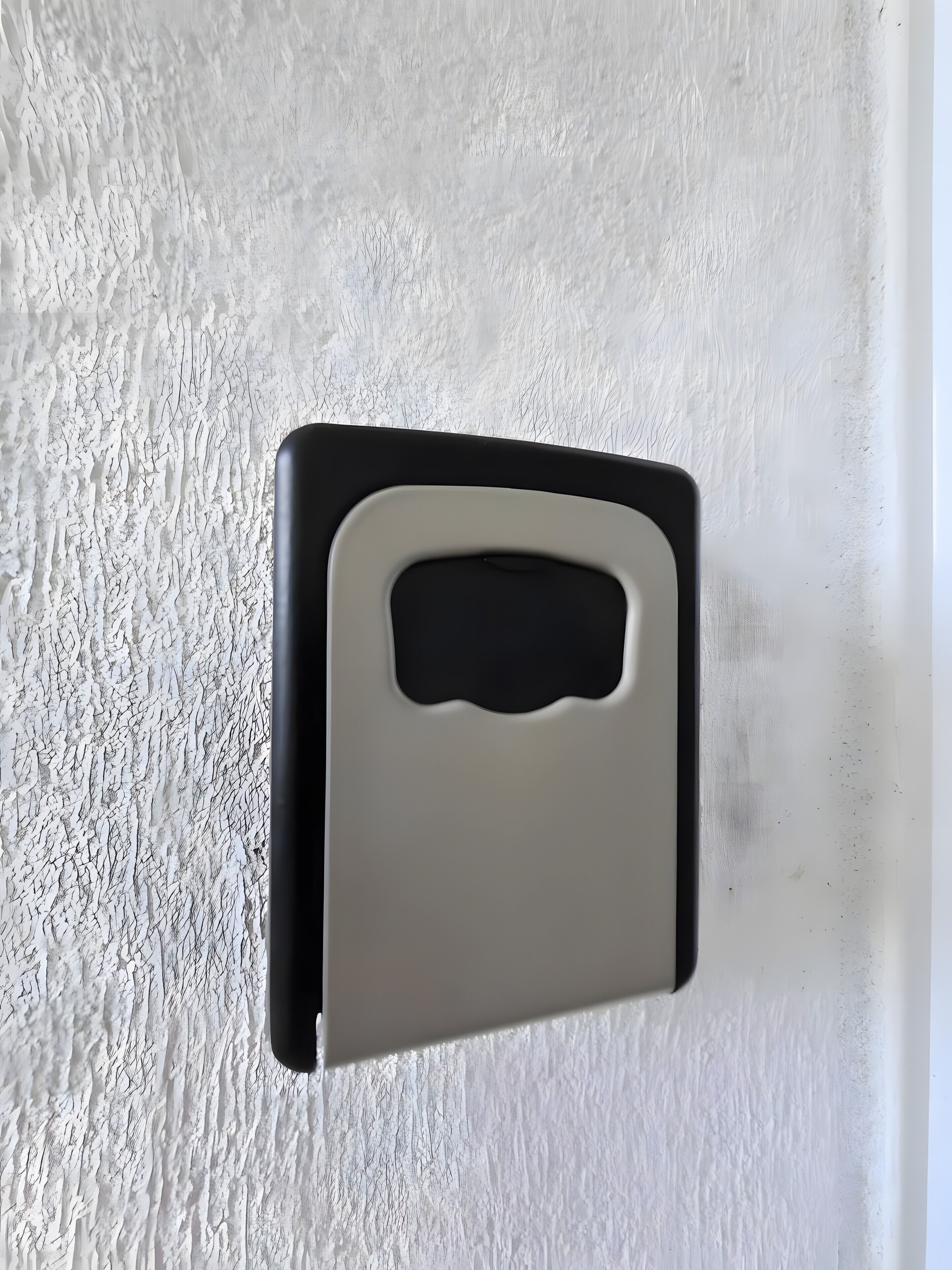 Un mur blanc à texture, agrémenté d’un interphone noir et blanc.