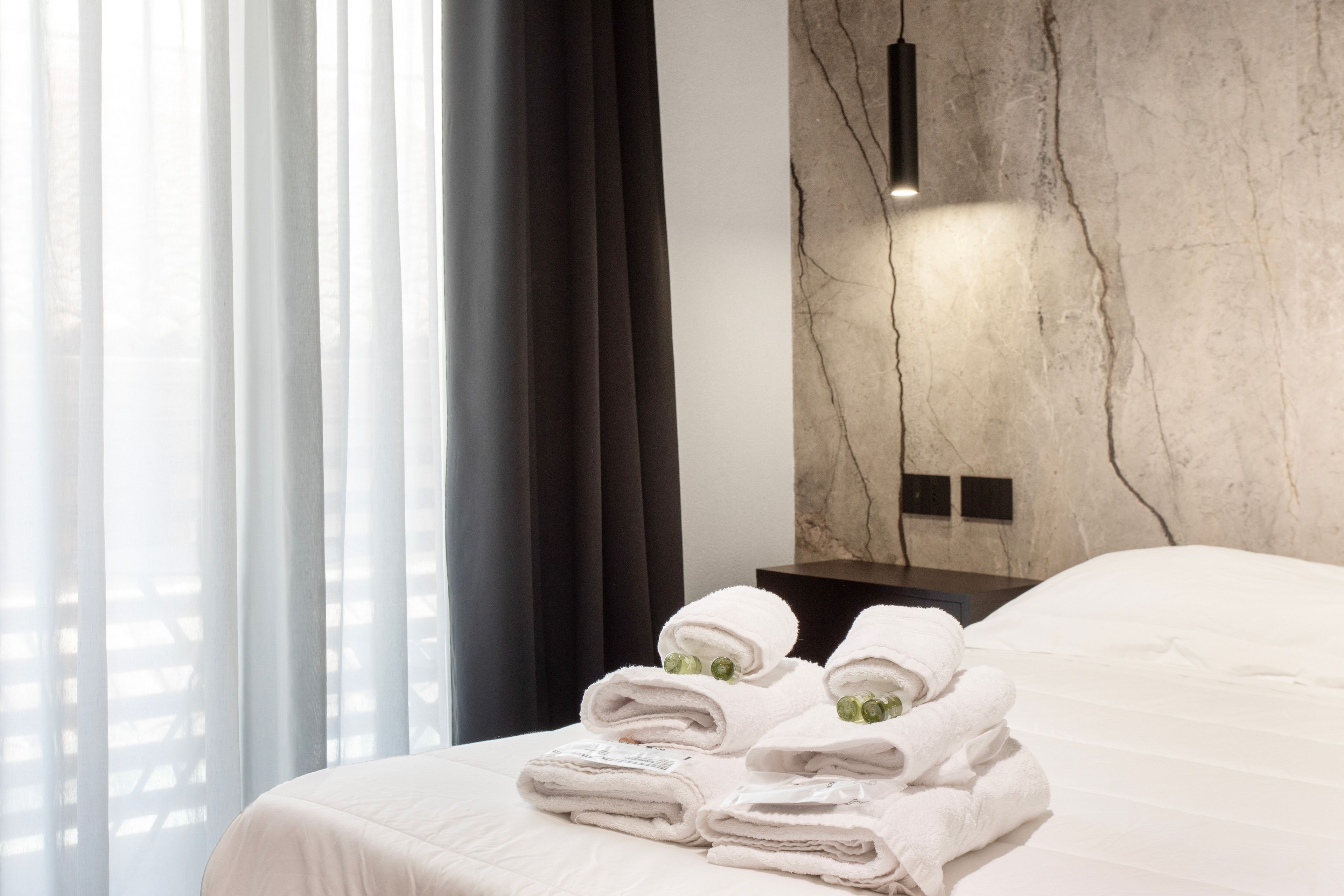A hotel room with a bed, a wall-mounted light, and a window with curtains.