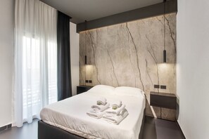 Un dormitorio moderno con una cama grande, una pared de mármol y dos luces fijadas a la pared.