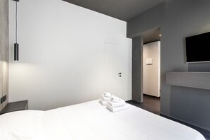 A hotel room with a neatly made bed, a flat-screen TV mounted on the wall, and a door leading to a hallway. - Bed and Breakfast 'Vicolo Del Fortino - Suite 105' with Balcony, Wi-Fi and Air Conditioning (Catania)
