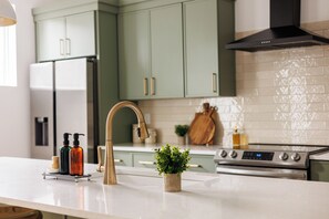 A modern kitchen with a white countertop, a gold faucet, and a stainless steel stove. - Nashville Rooftop Home with Hot Tub & Skyline Views (Nashville)
