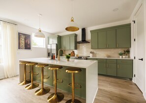 A modern kitchen with green cabinets, a white island with bar stools, and pendant lighting. - Nashville Rooftop Home with Hot Tub & Skyline Views (Nashville)
