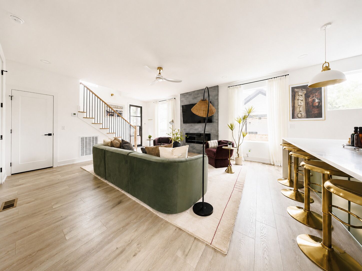 Una sala de estar moderna con un sofá verde, una chimenea, una escalera y una zona de cocina con taburetes de bar.