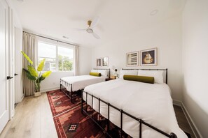 Ein Schlafzimmer mit zwei Einzelbetten, einem großen Fenster, einem Deckenventilator und Blick ins Freie.