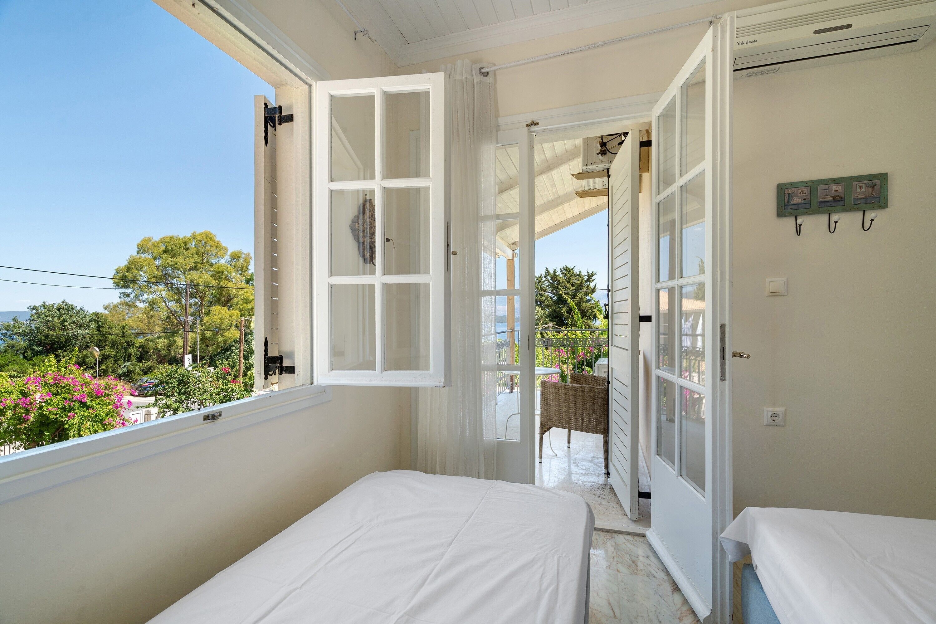 Quarto com duas camas, varanda e vista para árvores e flores.