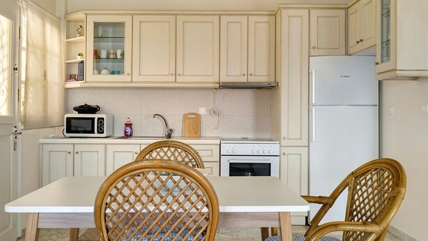 A kitchen with white cabinets, a microwave, a sink, a stove, and a refrigerator. There is a dining table with chairs. - Holiday Home 'Evans Terrace Suite' (Nikiana)