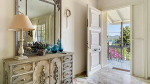 A room with a large mirror, a dresser with decorative items, and a door leading to a balcony with a view of greenery and mountains. - Holiday Home 'Evans Terrace Suite' (Nikiana)